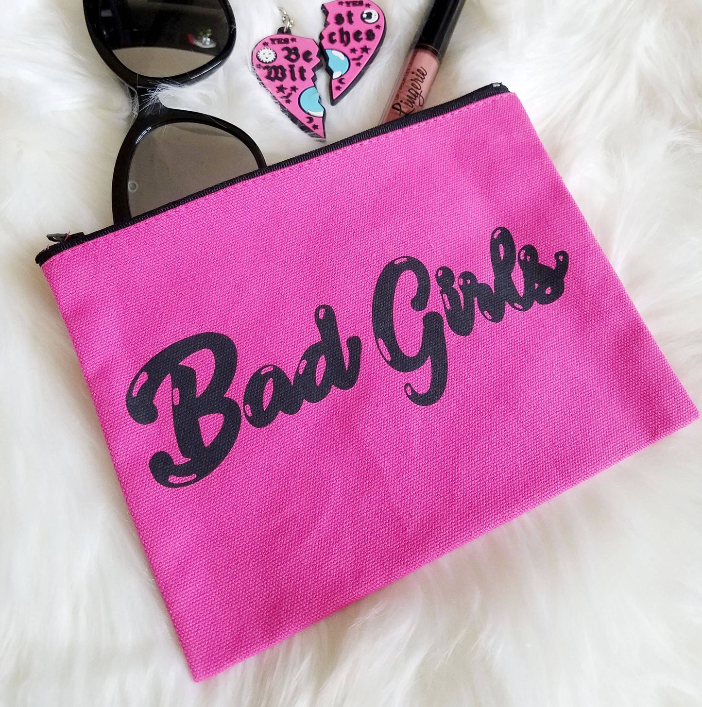 bad girls hot pink zipper pouch with black bubble letters shown displayed with sunglasses earrings and lipgloss
