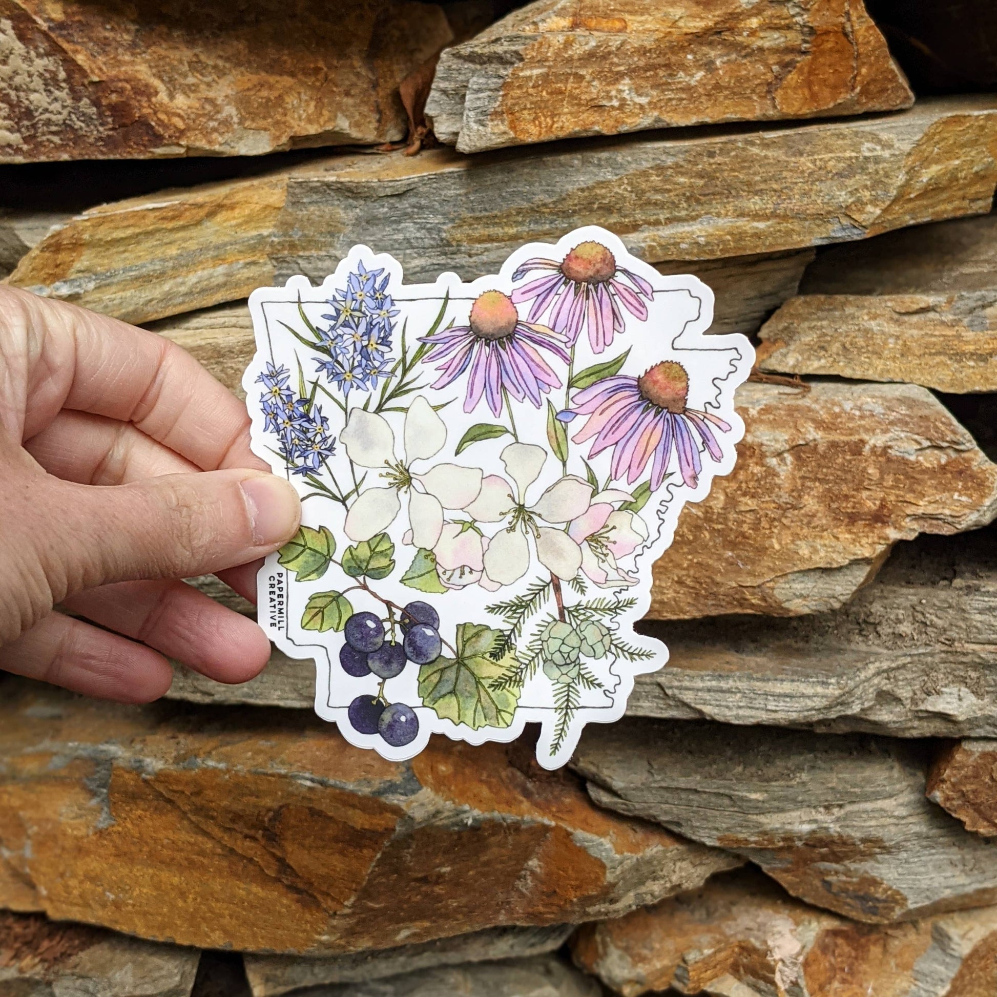 hand holding a vinyl sticker of the silhouette of the state of arkansas with watercolor botanicals