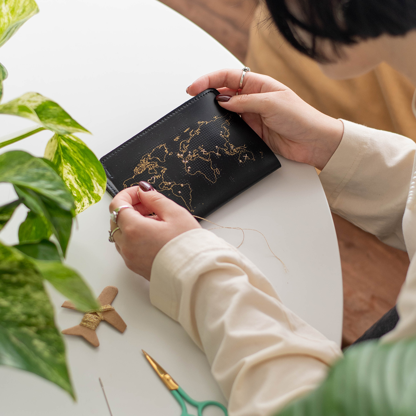 image of someone actively sewing stitching an x over the countries and areas they have visited on their black passport cover with gold thread