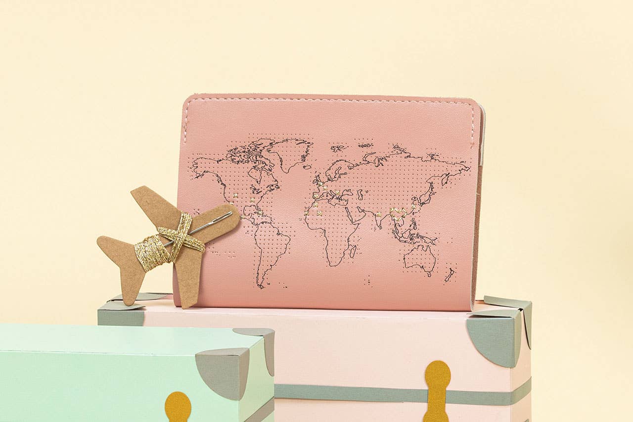 image of pink passport cover with the perforated world map and some golden cross stiches over the countries visited