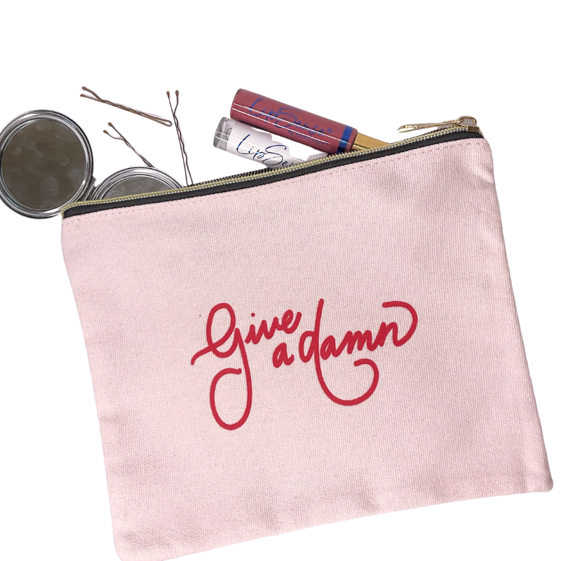 give a damn zipper pouch light pink canvas zipper pouch with cursive give a damn written on top in red with makeup displayed