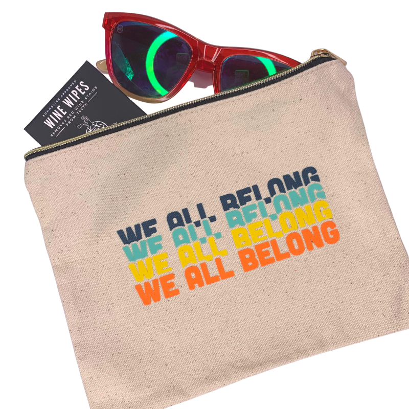 we all belong zipper pouch natural unbleached canvas pouch with colorful we all belong design on top displayed with sunglasses and wine wipes